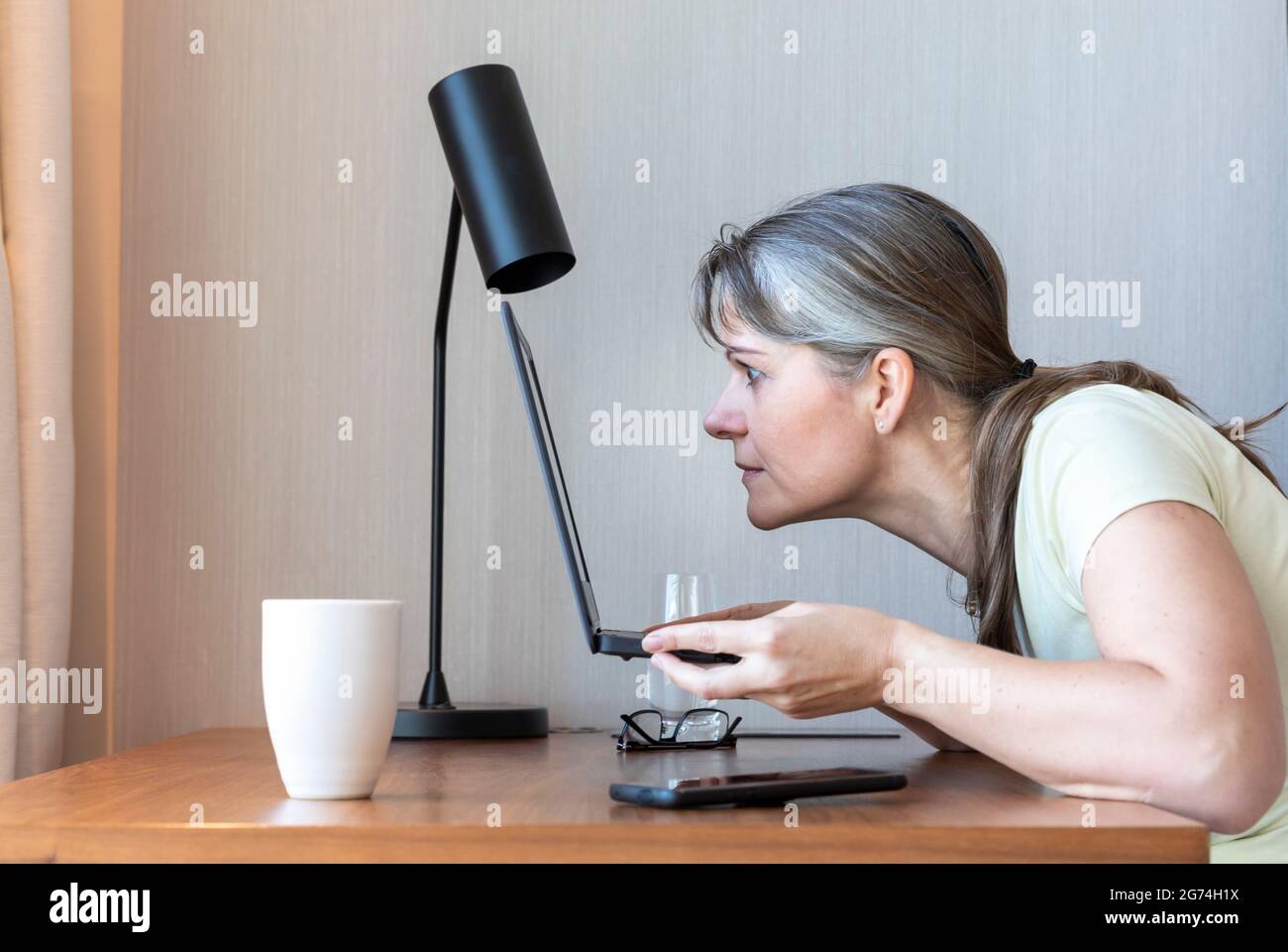 Eine Frau mit einem schlechten Sehvermögen, die in ihrem Laptop arbeitet und Schwierigkeiten hat zu sehen Stockfoto