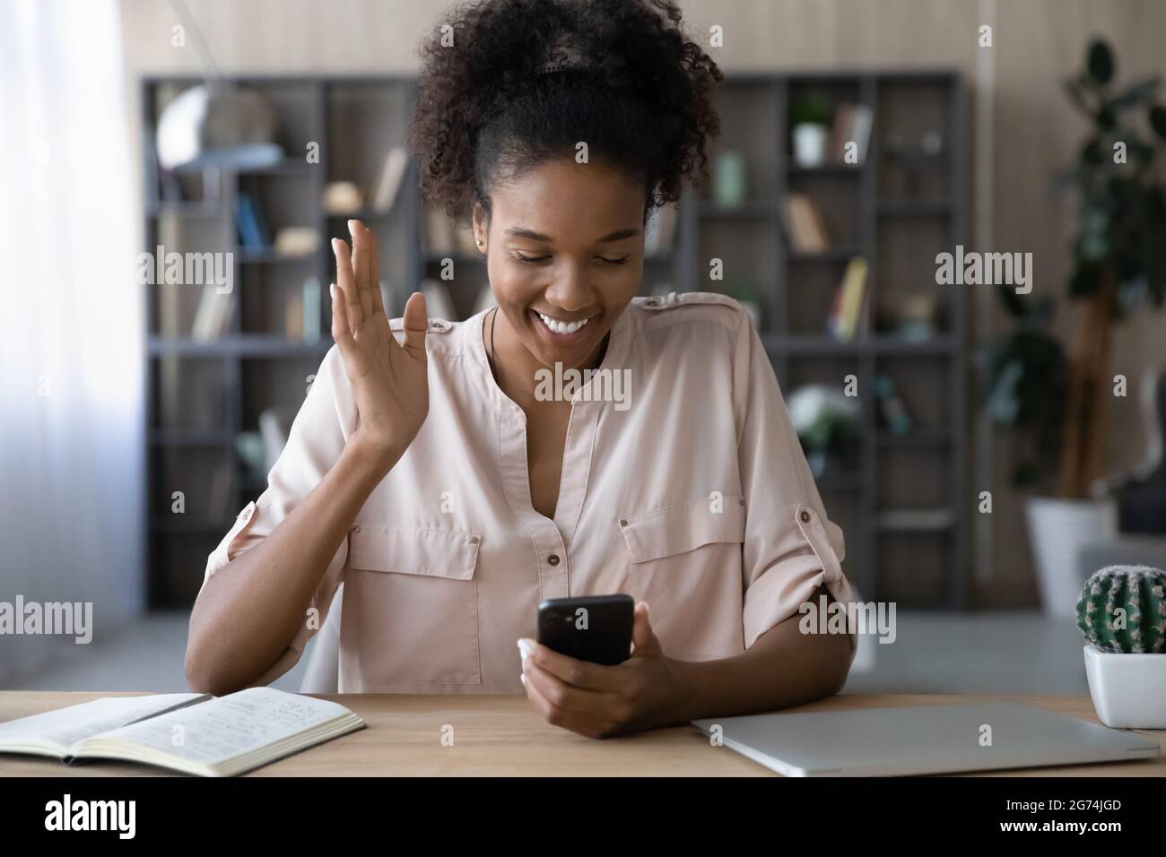 Lächelnde afroamerikanische Frau winkt Hand, hält Smartphone, chattet online Stockfoto