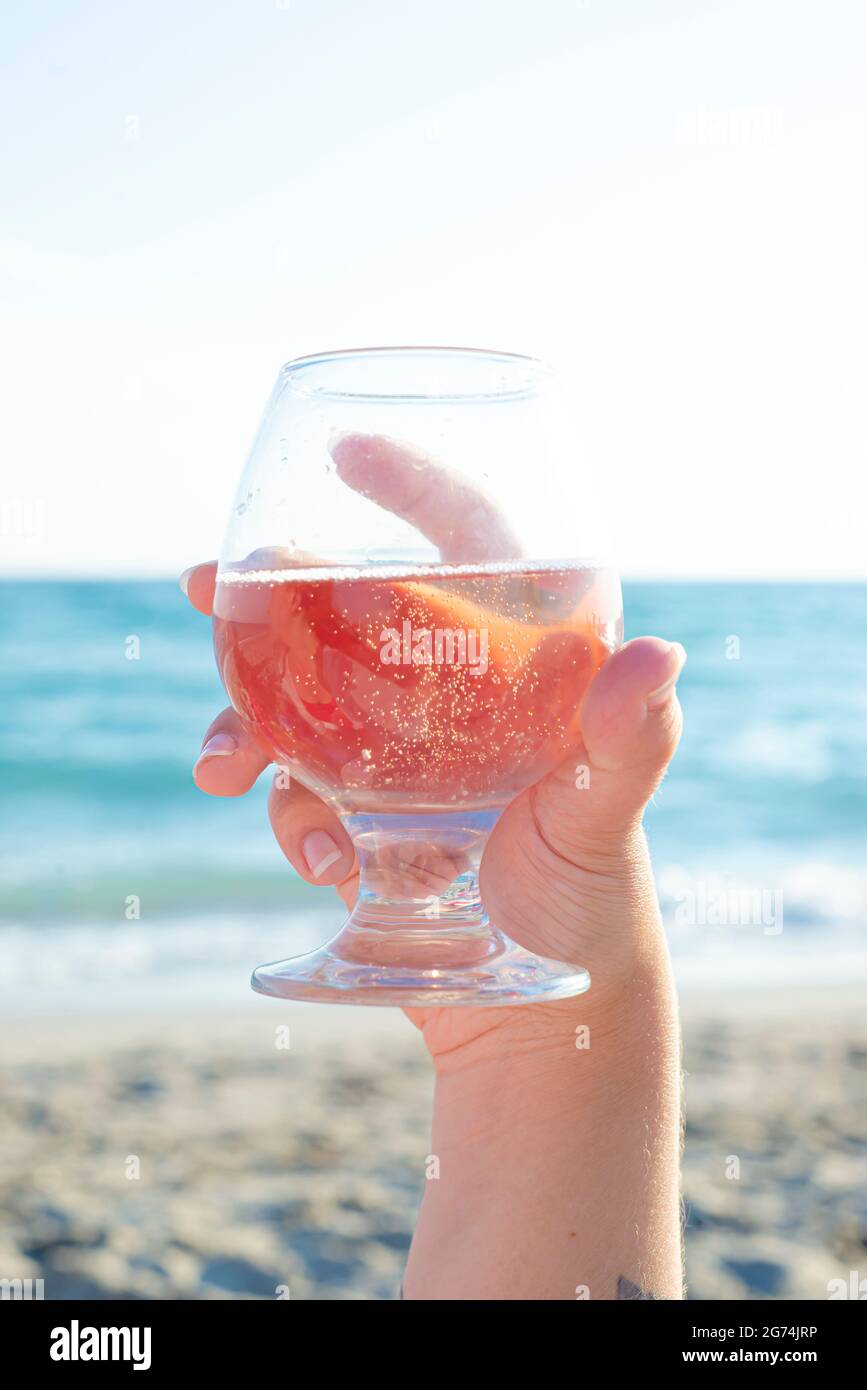 Weinglas mit Rosenwein in weiblicher Hand auf dem Hintergrund des Meeres Sandstrand. Horizont. Stockfoto