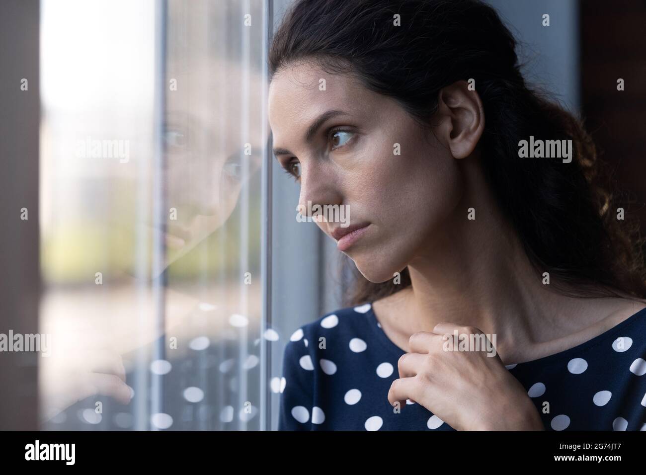 Traurige, nachdenkliche hispanische Frau, die tief nachdenklich aus dem Fenster schaut Stockfoto