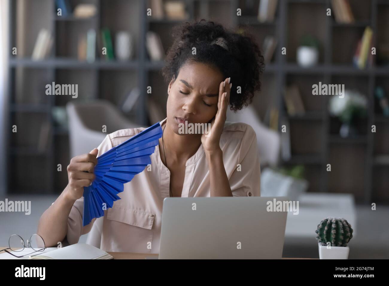 Müde afroamerikanische Frau winkt Papierfächer am Arbeitsplatz Stockfoto