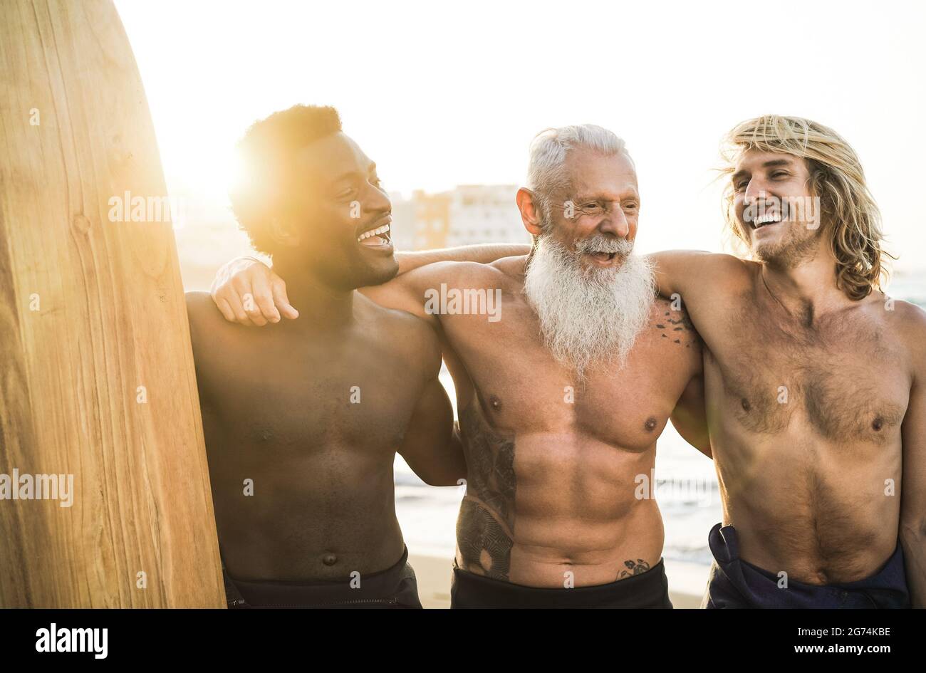 Surfer-Freunde mit mehreren Generationen, die nach der Surfstunde am Strand Spaß haben – konzentrieren Sie sich auf das Gesicht eines älteren Mannes Stockfoto