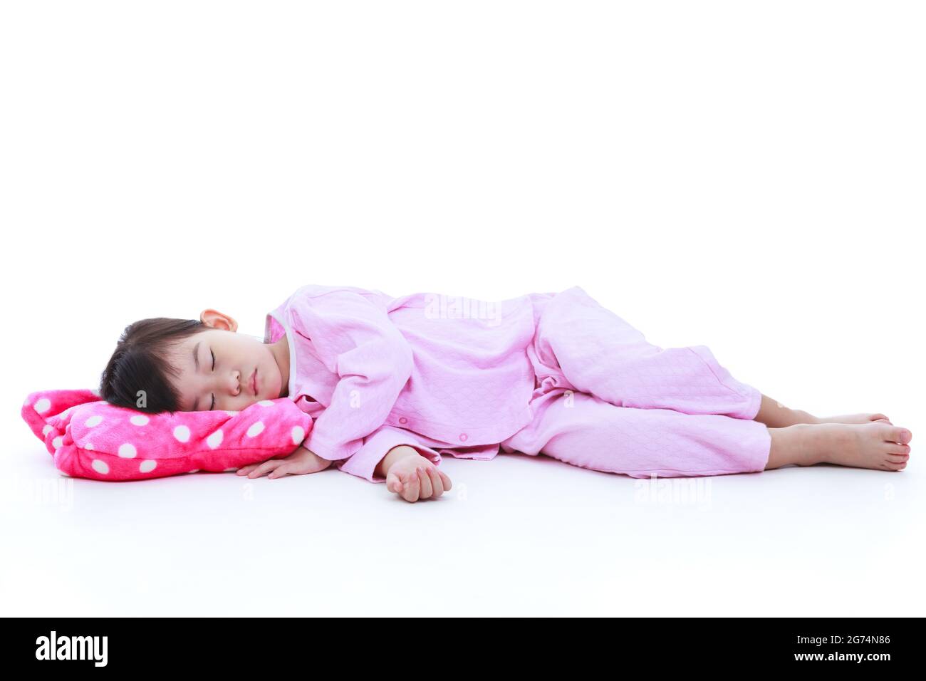 Ganzkörper. Gesundes Kinderkonzept. Kleines asiatisches Kind schläft friedlich. Liebenswert Mädchen in rosa Schlafanzug unter ein Nickerchen. Isoliert auf weißem Hintergrund. Stockfoto