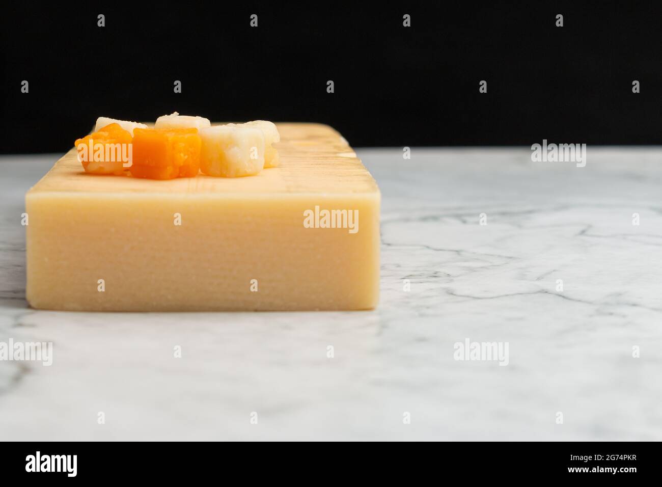 Nahaufnahme eines gelben Cheddar-Käses mit kleinen Käsequadraten auf einer Marmoroberfläche Stockfoto