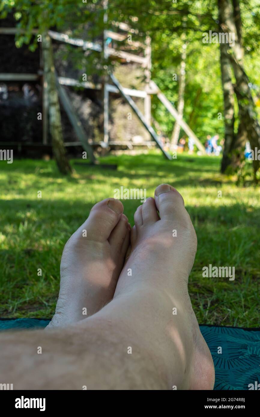 Persönliche Sicht auf die Beine und Füße eines Mannes, der sich im Stadtpark auf dem Rasen entspannt. Foto aufgenommen an einem sonnigen Tag bei Tageslicht. Stockfoto