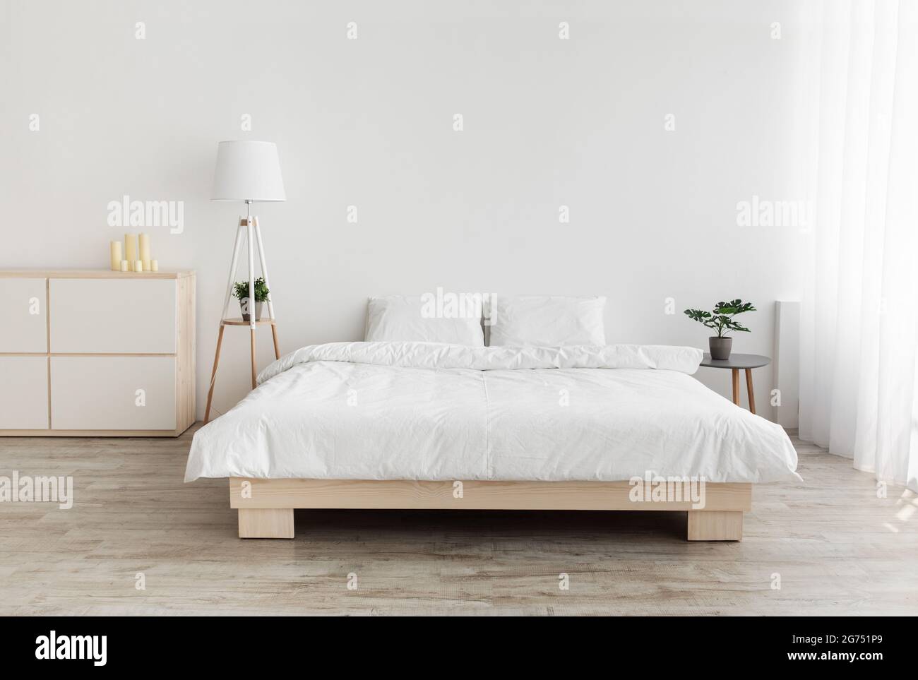 Echtes Foto des Schlafzimmers im einfachen Stil. Großes Bett mit Kissen, Lampe und Möbeln, weiße Wand, leerer Raum Stockfoto