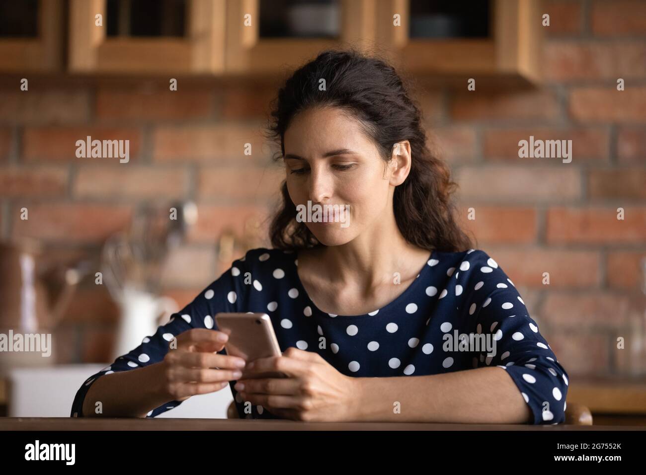 Fokussierte lateinische Frau, die Text auf dem Handy-Bildschirm in der Küche liest Stockfoto