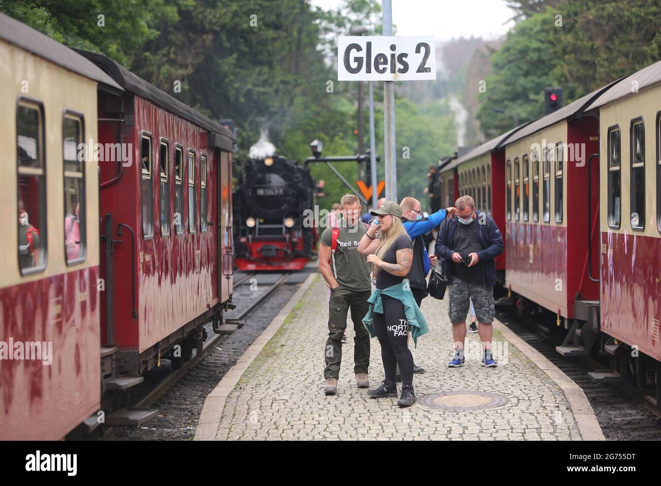 Schierke, Deutschland. Juli 2021. Passagiere stehen am Bahnhof und steigen in den Zug der Harzer Schmalspurbahn HSB. Die HSB führt den Sommerflugplan wieder uneingeschränkt aus. Zuvor wurden die Zugverbindungen für sieben Monate fast vollständig eingestellt. Mit Beginn der Ferienzeit steigen auch die Passagierzahlen wieder an. Quelle: Matthias Bein/dpa-Zentralbild/ZB/dpa/Alamy Live News Stockfoto