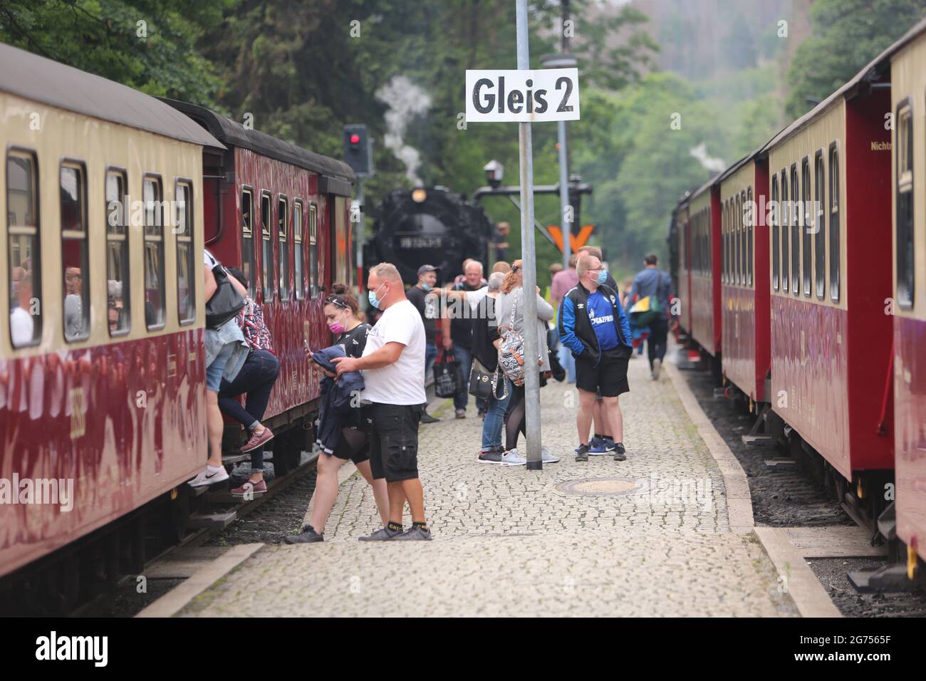 Schierke, Deutschland. Juli 2021. Passagiere stehen am Bahnhof und steigen in den Zug der Harzer Schmalspurbahn HSB. Die HSB führt den Sommerflugplan wieder uneingeschränkt aus. Zuvor wurden die Zugverbindungen für sieben Monate fast vollständig eingestellt. Mit Beginn der Ferienzeit steigt auch die Zahl der Passagiere wieder an. Quelle: Matthias Bein/dpa-Zentralbild/dpa/Alamy Live News Stockfoto