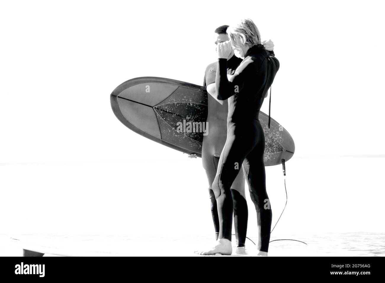 Surfer aller Altersgruppen tragen Surfbretter zum Ufer des Llangennith Beach auf der Gower Peninsula. Monochromes Bild, das Aktivitäten im Freien zeigt. Stockfoto