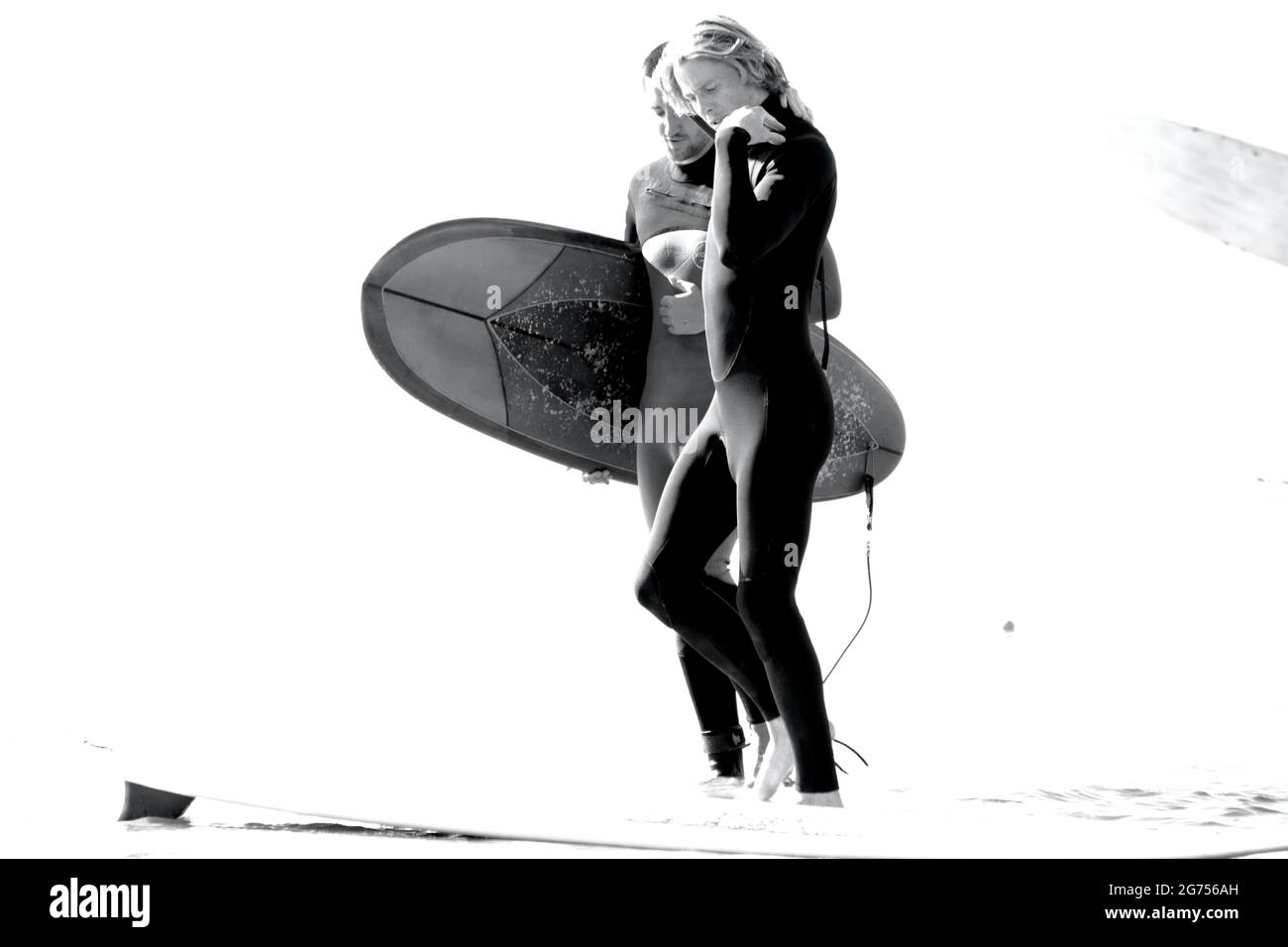 Surfer aller Altersgruppen tragen Surfbretter zum Ufer des Llangennith Beach auf der Gower Peninsula. Monochromes Bild, das Aktivitäten im Freien zeigt. Stockfoto