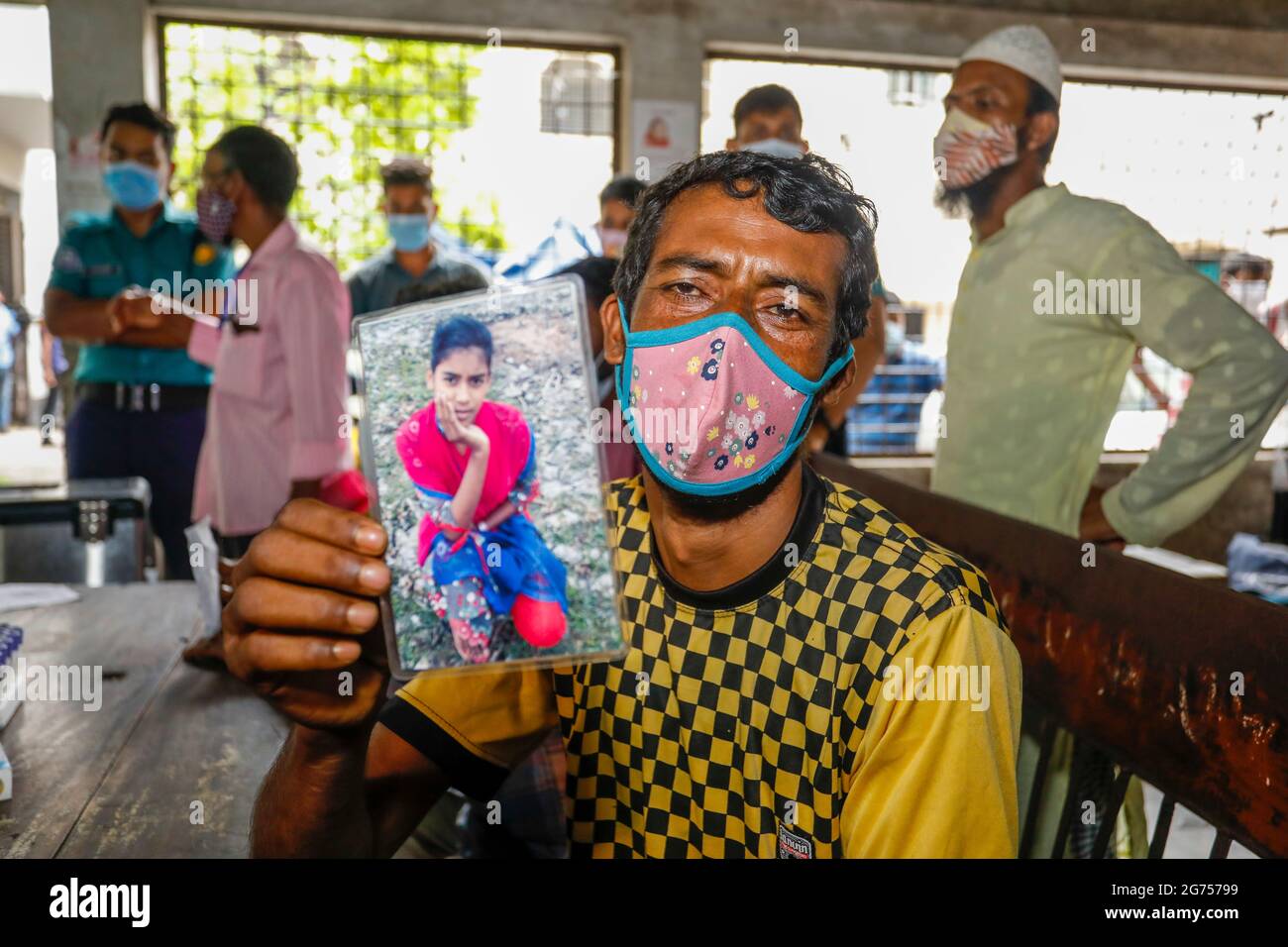 Ein Vater hält das Foto seiner Tochter im Krankenhaus der medizinischen Hochschule Dhaka, während medizinische Beamte Blutproben von den Verwandten des Opfers sammeln Stockfoto