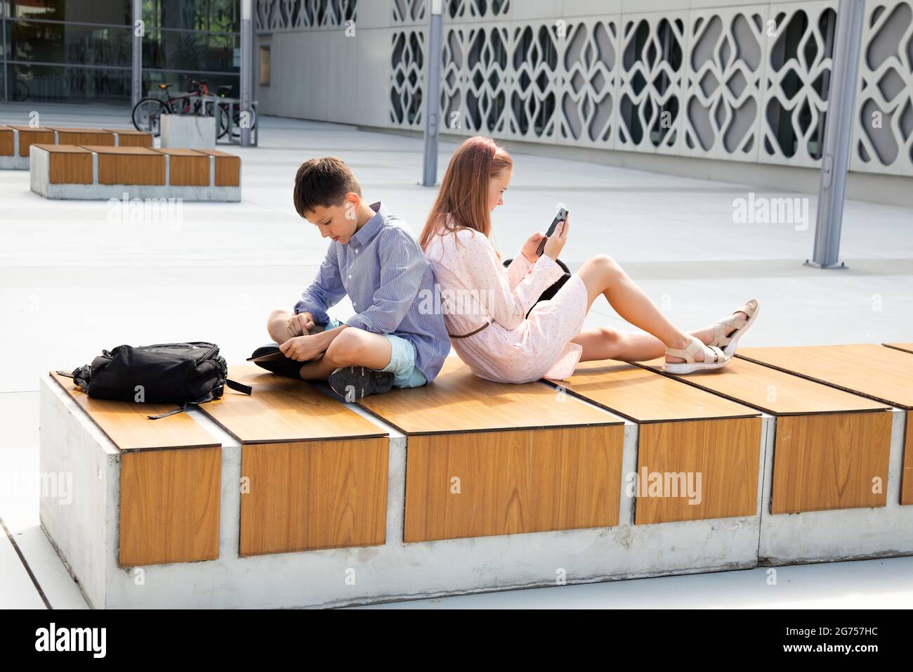 Kinder Schüler lehnen sich auf dem Schulhof zurück und machen Hausaufgaben mit mobilen Geräten Stockfoto