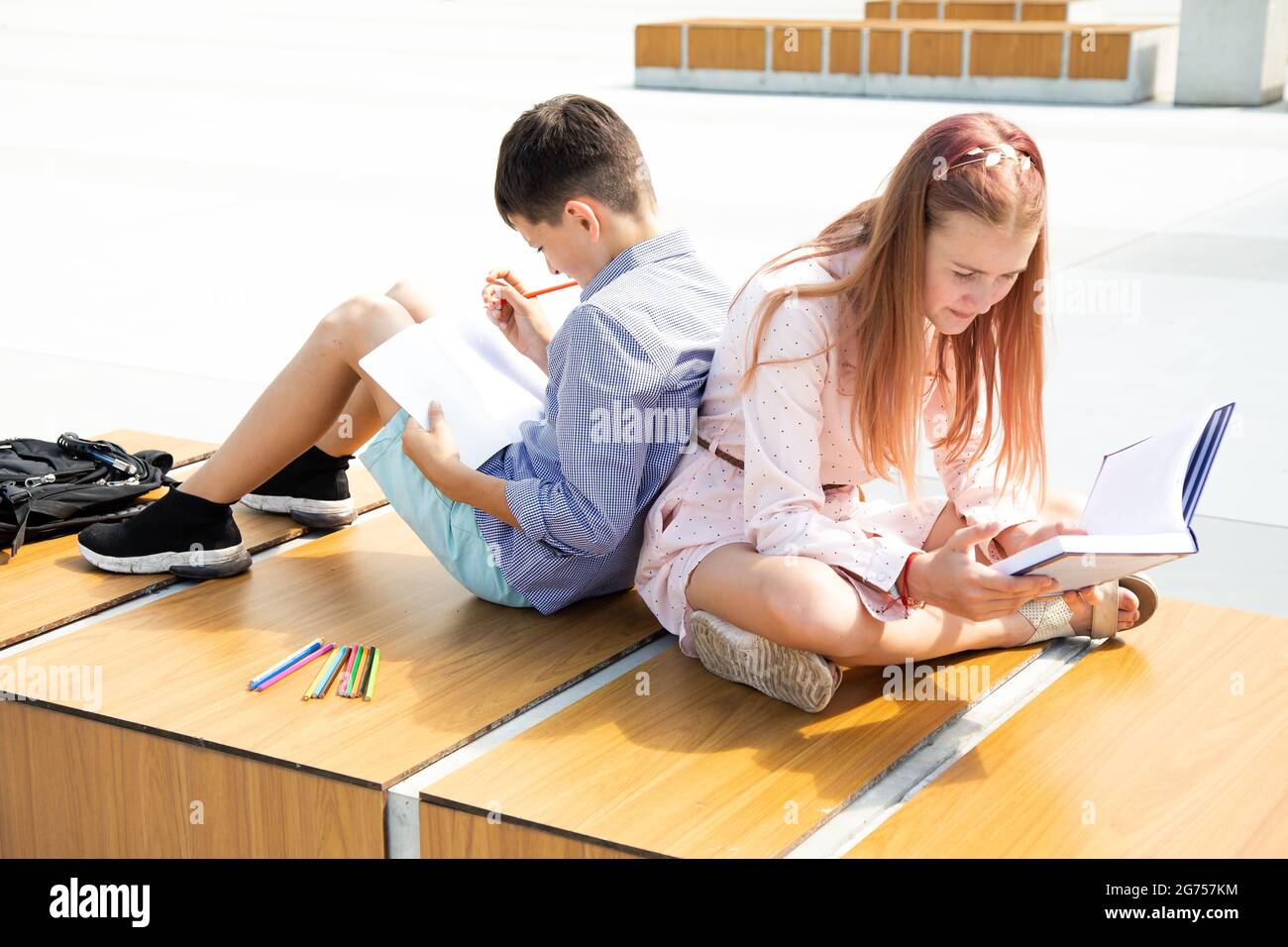 Schüler Mädchen und Jungen Jugendliche 11 Jahre alt studieren auf dem Schulhof, sitzen auf der Bank im Schulhof, lesen Buch und schreiben in Notebook Stockfoto
