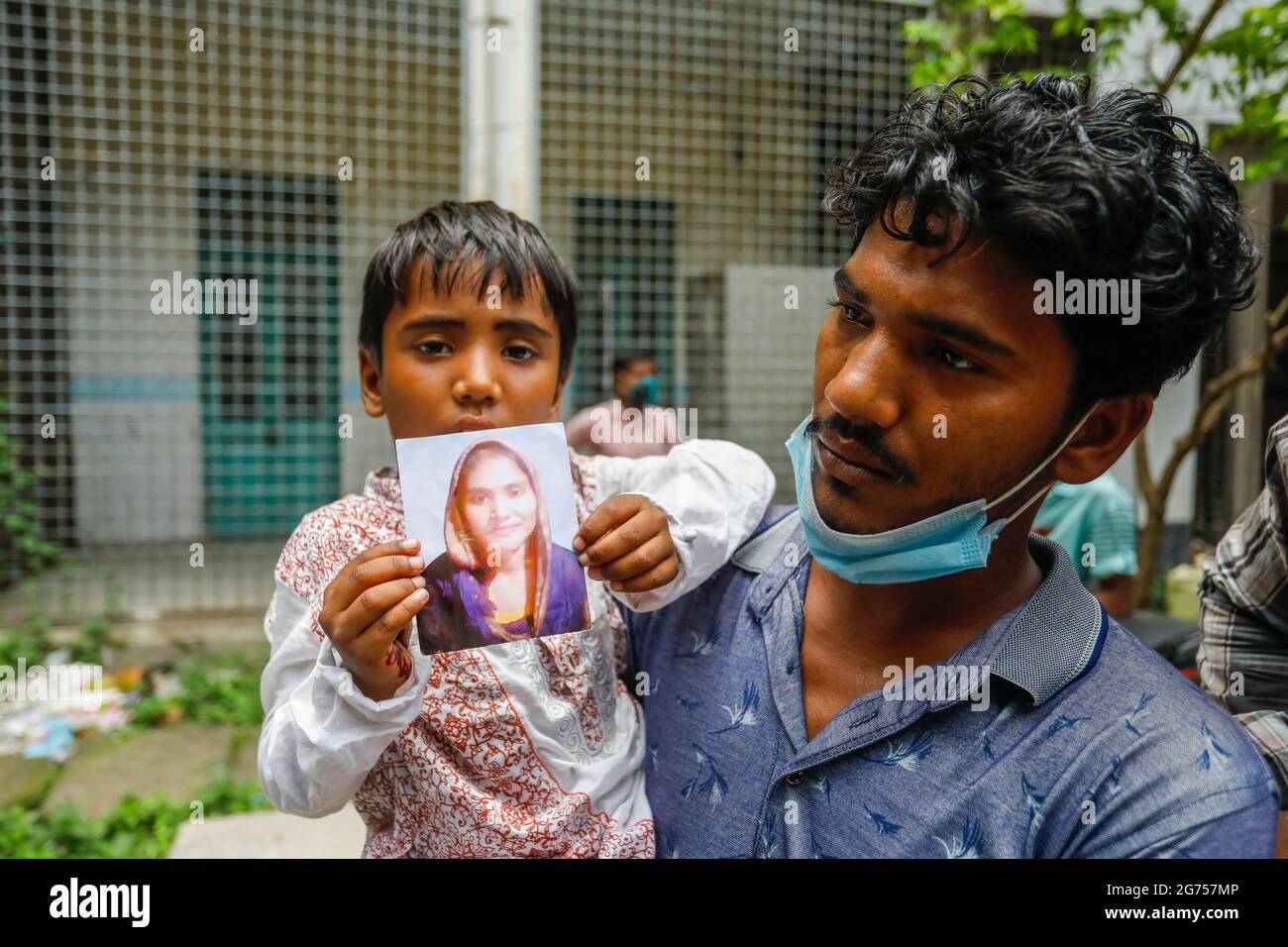 Ein Kind, das das Foto seiner Mutter im Krankenhaus der Dhaka Medical College hält, während medizinische Beamte Blutproben von den Verwandten der Opfer sammeln o Stockfoto