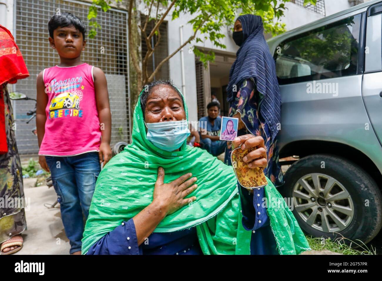 Eine Frau, die das Foto ihrer Schwester im Krankenhaus der Dhaka Medical College hält, während medizinische Beamte Blutproben von den Verwandten der Opfer sammeln o Stockfoto