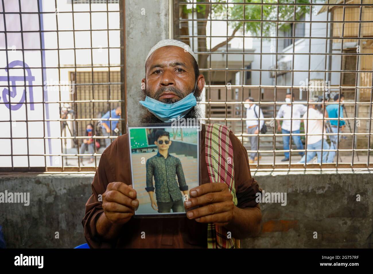 Ein Vater hält das Foto seines Sohnes im Krankenhaus der medizinischen Hochschule Dhaka, während medizinische Beamte Blutproben von den Verwandten der Opfer von sammeln Stockfoto