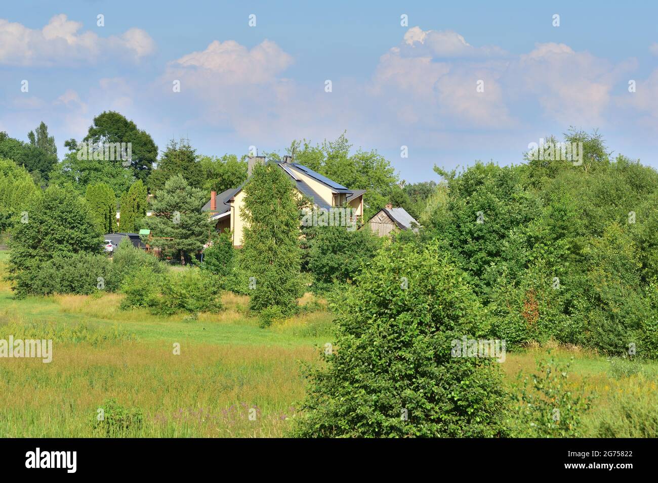 Blick auf das Anwesen der Einfamilienhäuser zwischen Bäumen und grünen Wiesen. Sommer. Stockfoto
