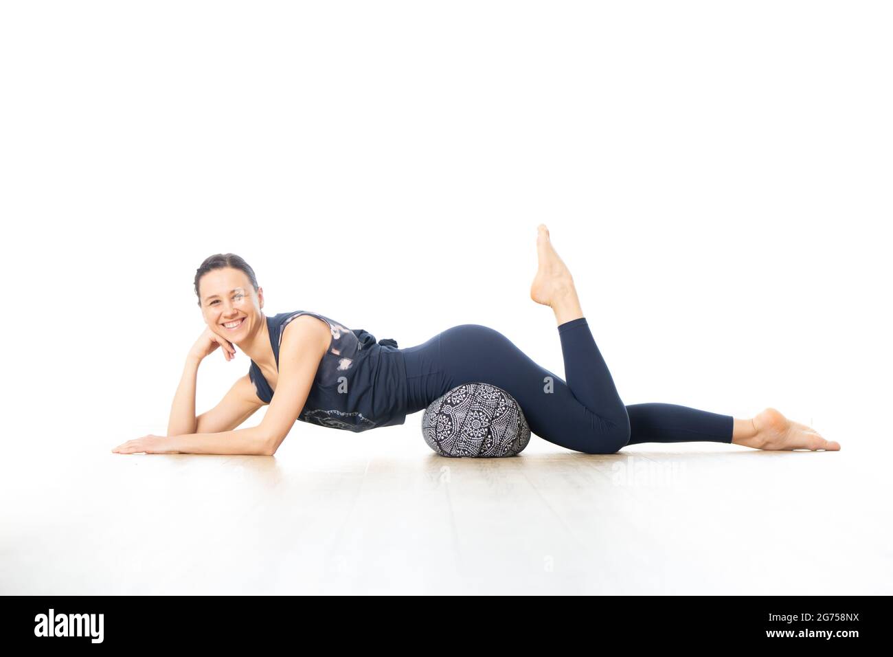 Erholendes Yoga mit einem Aufpolster. Junge sportliche weibliche Yogalehrerin im leuchtend weißen Yogastudio, auf Polsterkissen liegend, dehnend, smilling Stockfoto