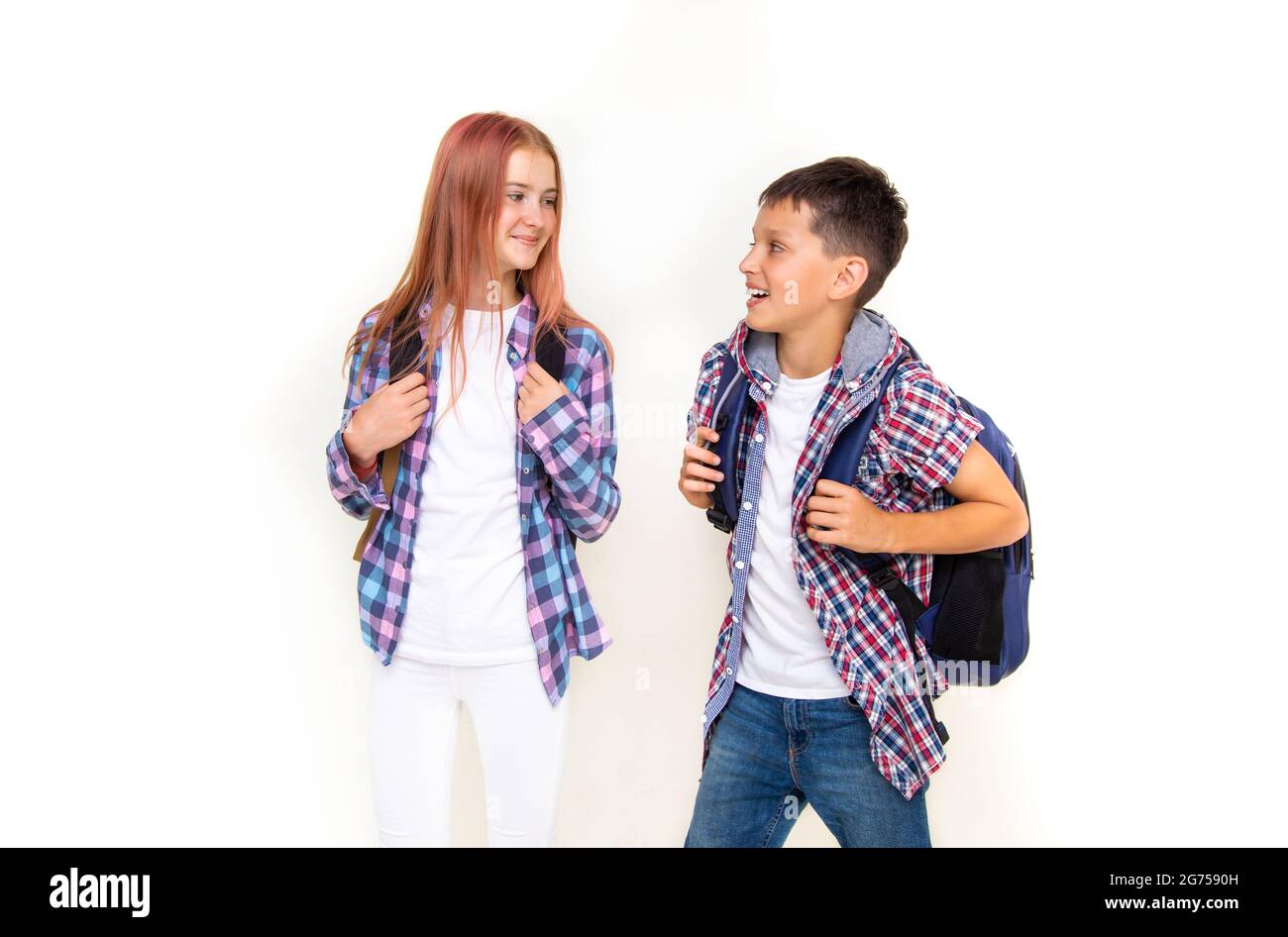 Junge und Mädchen Teenager 11 Jahre alt Schuljunge und Schülerin, Blick auf einander auf weißem Hintergrund mit Rucksäcken und lächelnd. Gekleidet in karierten Sh Stockfoto