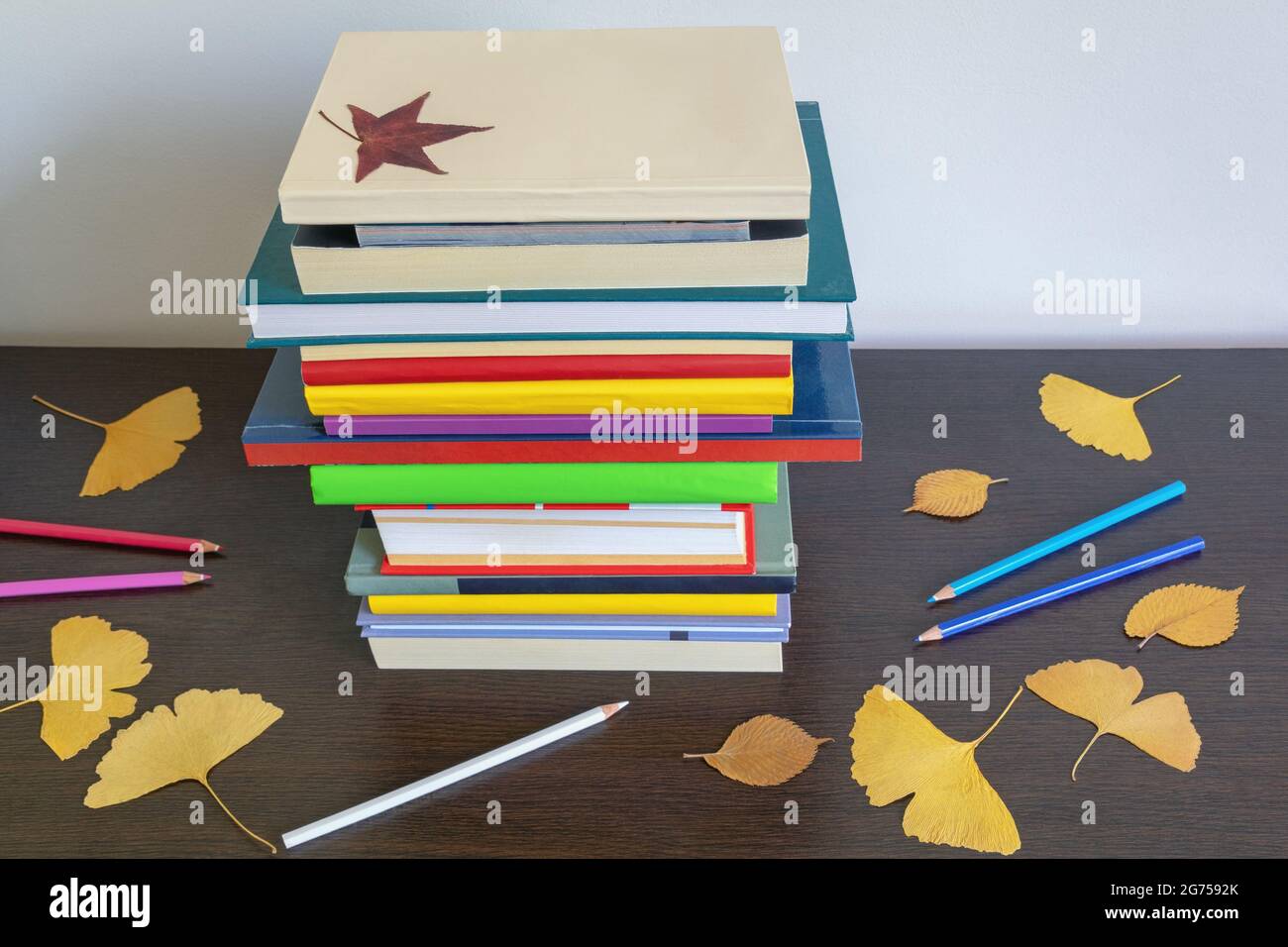 Schulkonzept. Stapel von verschiedenen Büchern, Herbstblättern und Buntstiften auf dem Tisch Stockfoto