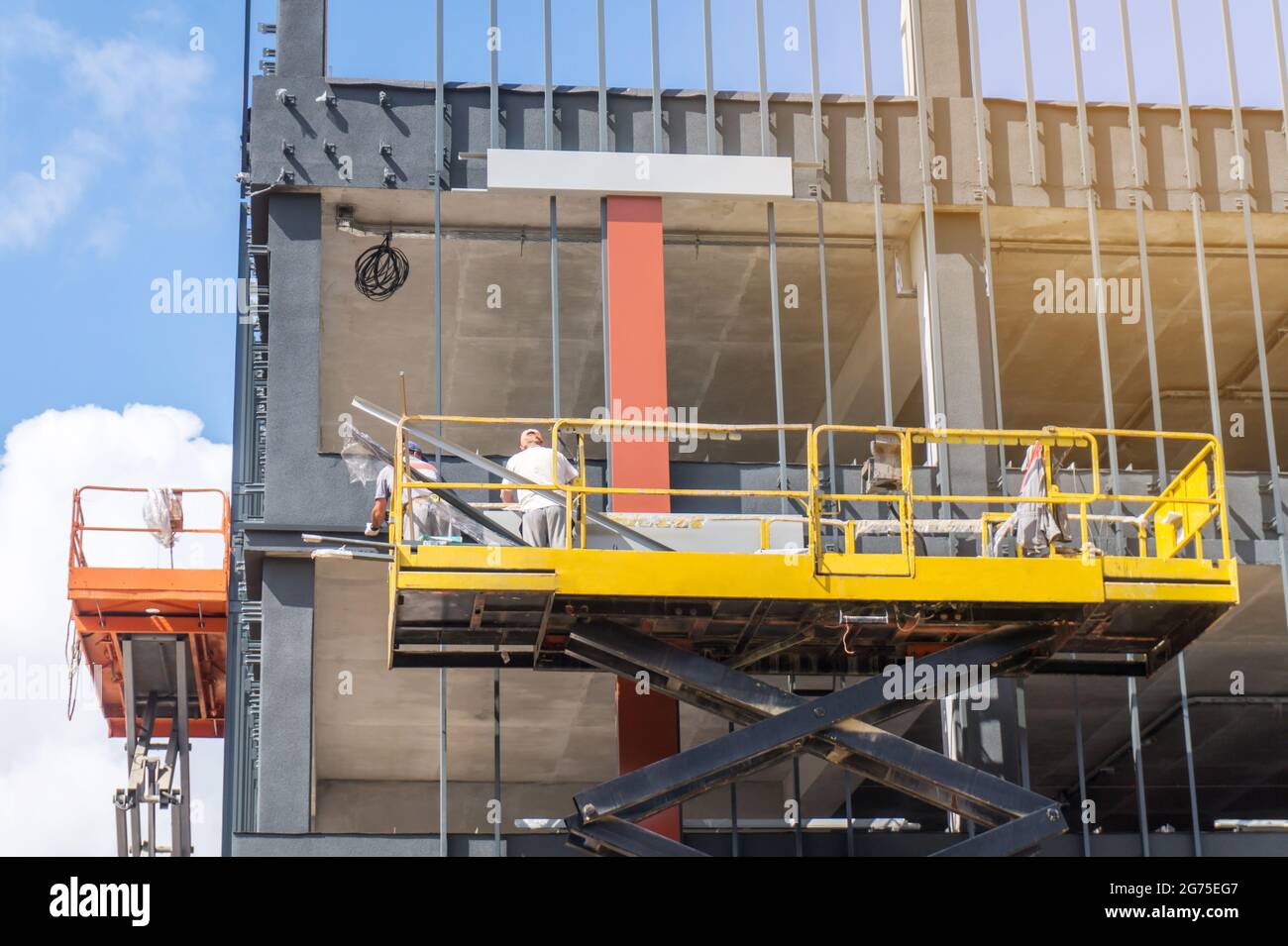 Bauarbeiter auf einer Scherenhubbühne auf einer Baustelle, die an der Fassade eines neuen Geschäftsgebäudes arbeiten Stockfoto