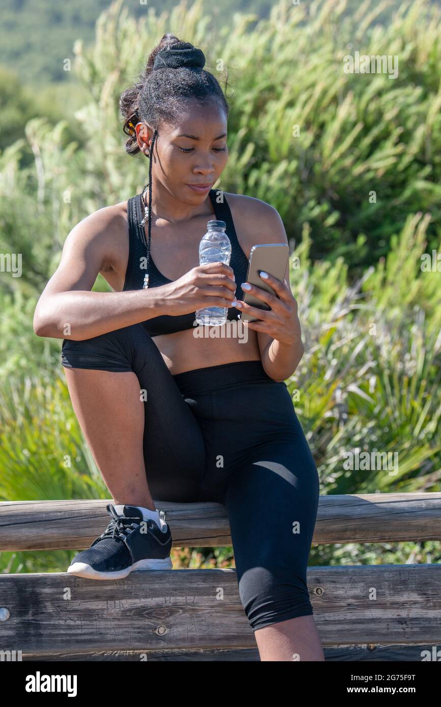 Fokussierte afroamerikanische Frau, die nach dem Training in einer Pause ihr Telefon überprüft Stockfoto