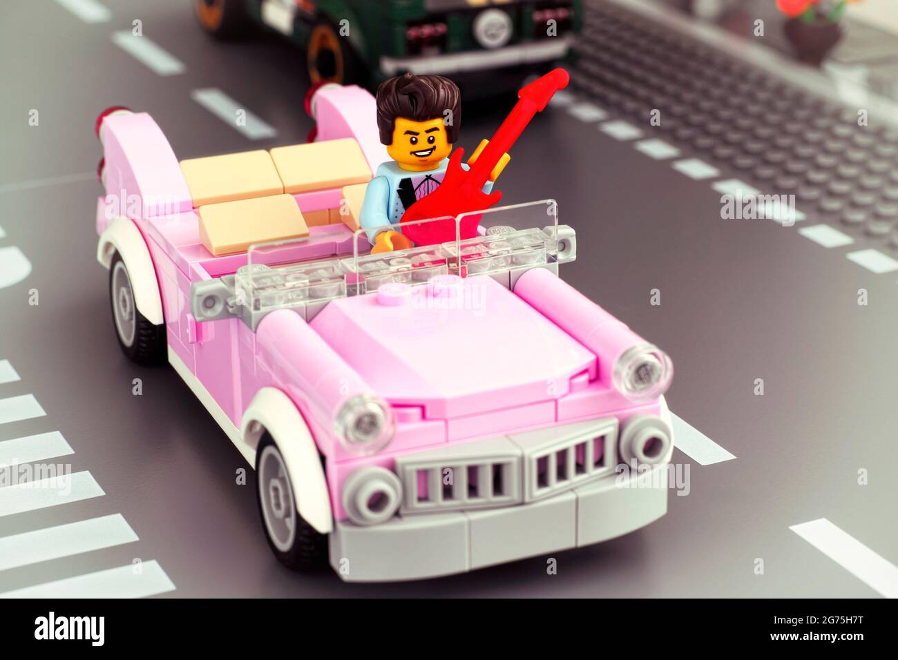 Tambov, Russische Föderation - 22. Januar 2020 Lego Rock-n-Roll-Star-Minifigur mit Gitarre, die ein rosafarbenes Cabriolet im Stil der 1950er Jahre auf der Straße antreibt. Stockfoto