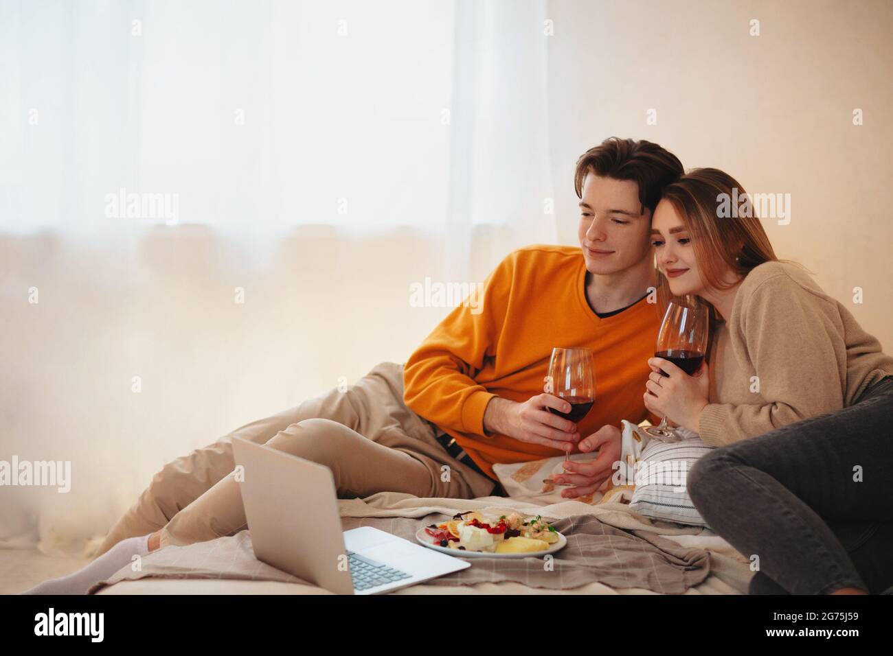 Junger Mann und Frau umarmen und genießen Rotwein während romantischen Date zu Hause Stockfoto