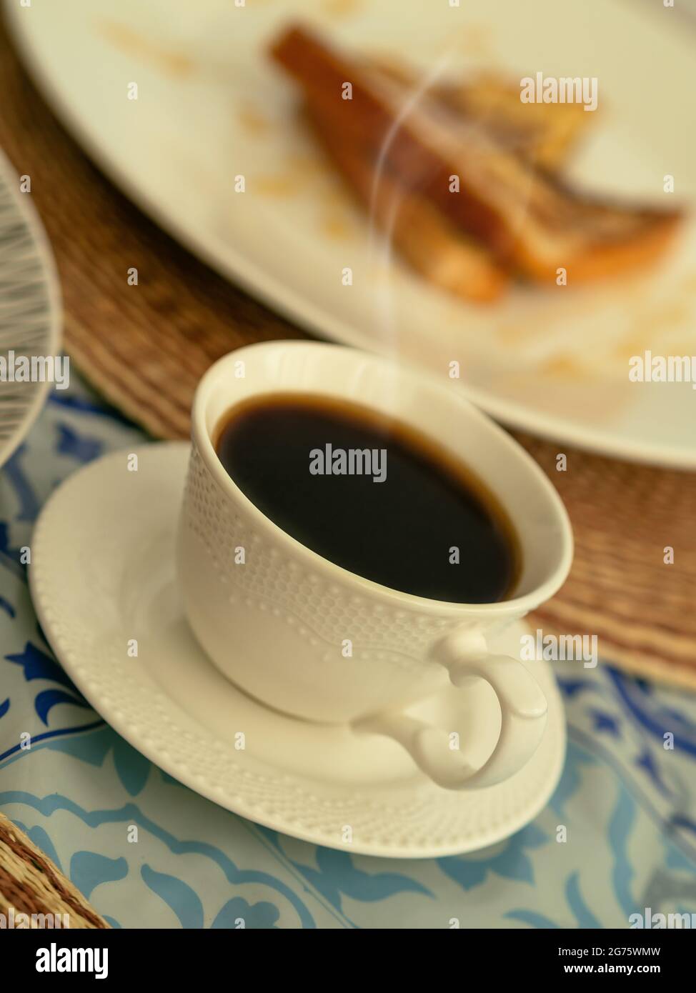 Eine weiße Tasse dampfenden schwarzen Kaffee, begleitet von französischem Toast zum Frühstück oder Brunch Stockfoto