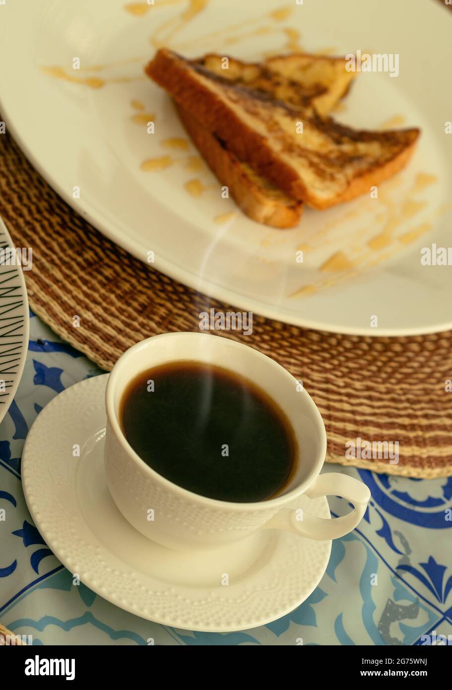 Eine weiße Tasse dampfenden schwarzen Kaffee, begleitet von französischem Toast zum Frühstück oder Brunch Stockfoto