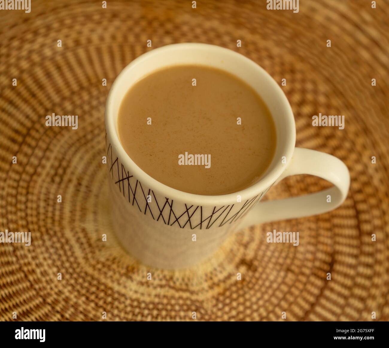 Kaffee mit Milch und Zimt in einem Becher auf einer braun gewebten Tischdecke Stockfoto