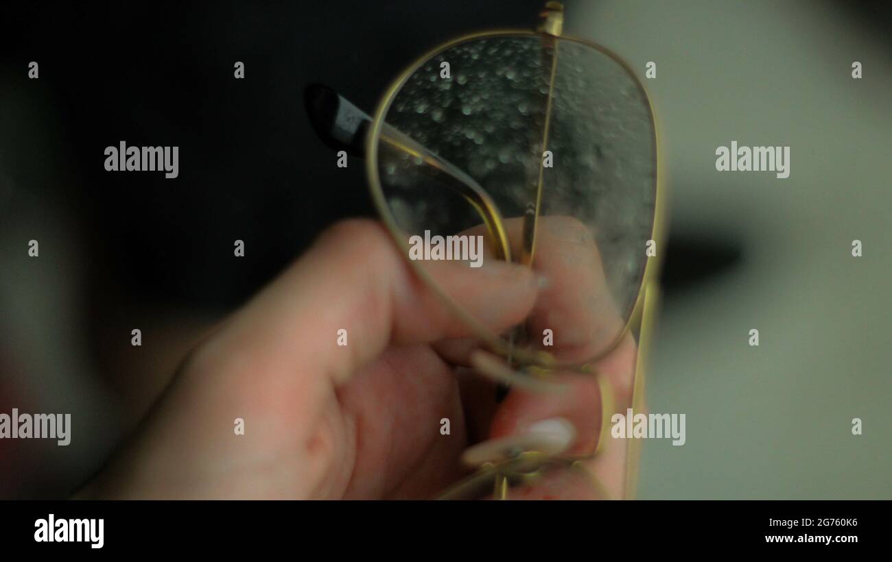 Eine Nahaufnahme einer weiblichen Hand, die eine mit Regentropfen bedeckte Fliegerbrille hält Stockfoto