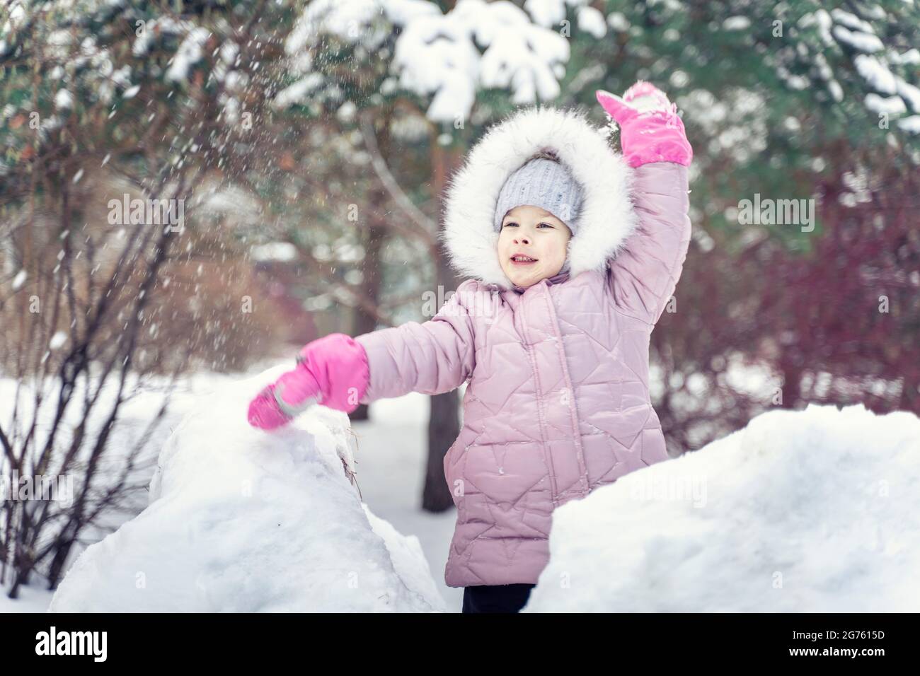 Lächelnd glücklich Kind Mädchen in warmen rosa Winterkleidung wirft einen Schneeball im Winter Stockfoto