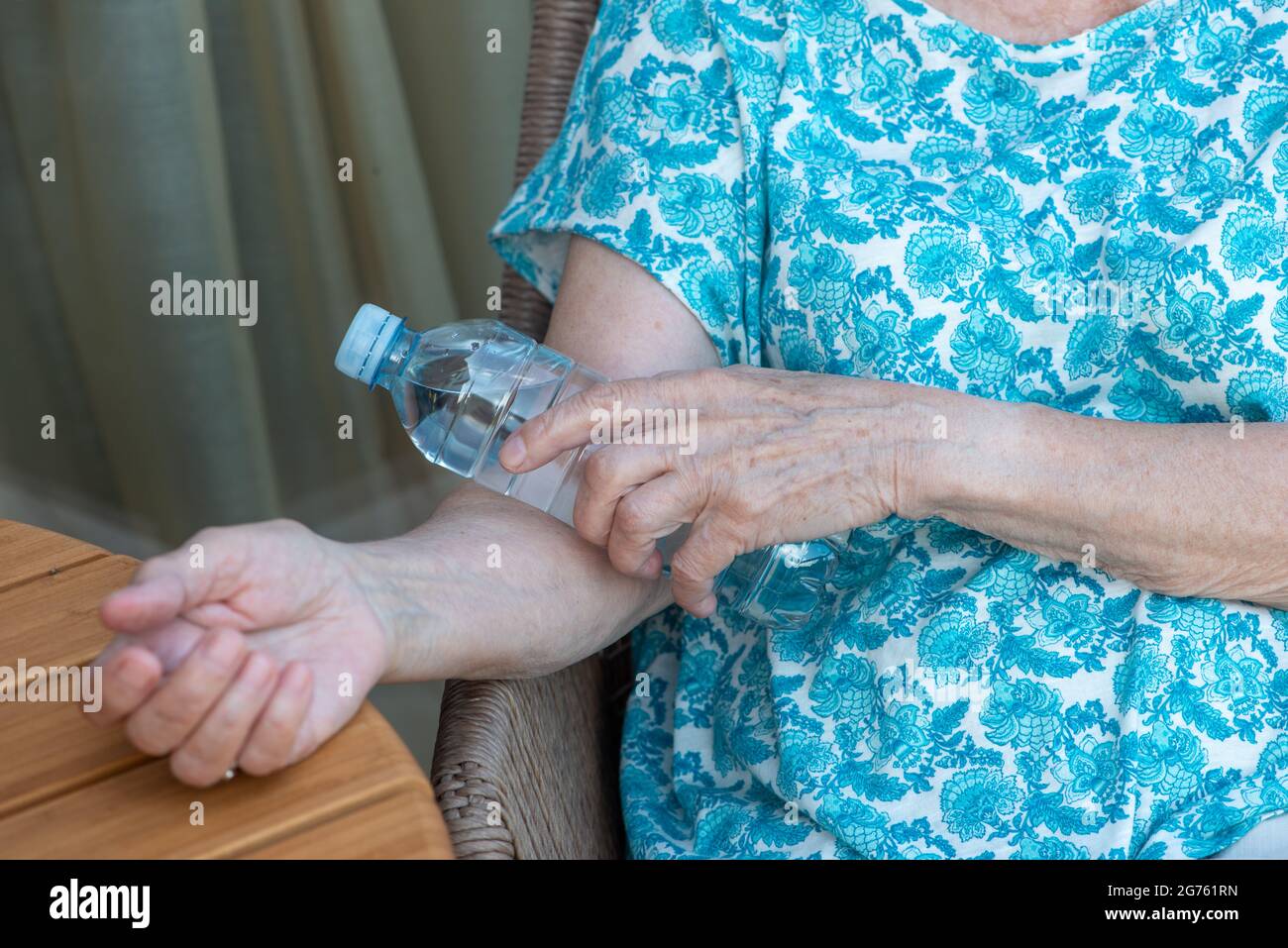 Die Hand der älteren Frau hält eine Flasche mit kaltem Wasser auf ihrem Ellenbogen. Wie man bei heißem Wetter kühl bleibt. Überstehen Sie die Hitze. Stockfoto