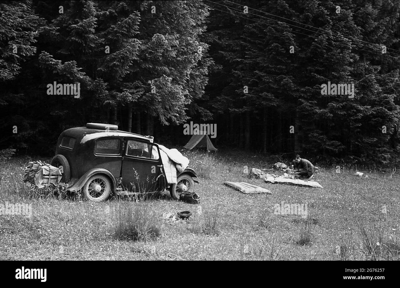1935, historisch, ein junger Mann, der nach dem Campen auf einem Feld am Waldrand in der Tiefebene der Sudeten unterwegs war, während er in einem Auto der damaligen Zeit (britisch) durch die Region des Sudentenlandes in der Tschechoslowakei vor dem 2. weltkrieg fuhr. Nur wenige Jahre später, 1938, wurde das Sudentenland, ein Gebiet mit überwiegend deutscher Bevölkerung, nach dem Münchner Abkommen von Deutschland besetzt. In dieser Zeit verfolgten sowohl Großbritannien als auch Frankreich mit Erinnerungen an die Schrecken des 1. Weltkrieges eine Politik, die als Beschwichtigung Deutschlands und ihrer nationalistischen Forderungen bekannt ist, Stockfoto