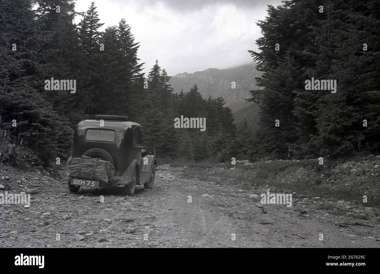 1935, historisch, ein Auto der Zeit, mit einem britischen Kennzeichen, gong auf einer felsigen, Schotterpiste hoch auf einem Waldgebiet der Sudeten oder Sudetenberge, Sudetenland, Tschechoslowakei. Sie sind der höchste Teil des so genannten Böhmischen Massivs, einer Reihe von Bergketten, die Teile mitteleuropas bedecken. Stockfoto