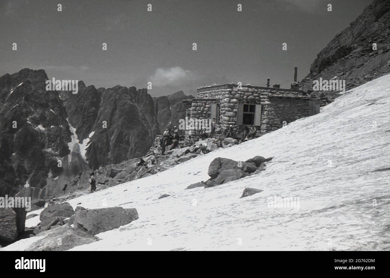 1935, historisch, Wanderer stehen vor einer aus Stein gebauten Berghütte auf den Sudetenbergen, Czechosolvakia. Solche Gebäude boten Wanderern und Wanderern Zuflucht und Schutz, als sie das Sudetengebirge begaben, nach dem das Sudetenland, das 1938 von Deutschland annektiert wurde, benannt ist. Sie bilden den höchsten Punkt des Böhmischen Massivs, einer Reihe von Gebirgszügen, die weite Teile des cemtralen Europas abdecken. Stockfoto