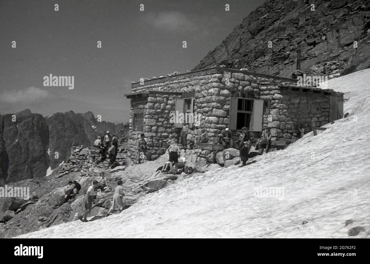 1935, historisch, Wanderer stehen vor einer aus Stein gebauten Berghütte auf den Sudetenbergen, Czechosolvakia. Solche Gebäude boten Wanderern und Wanderern Zuflucht und Schutz, als sie das Sudetengebirge begaben, nach dem das Sudetenland, das 1938 von Deutschland annektiert wurde, benannt ist. Sie bilden den höchsten Punkt des Böhmischen Massivs, einer Reihe von Gebirgszügen, die weite Teile des cemtralen Europas abdecken. Stockfoto