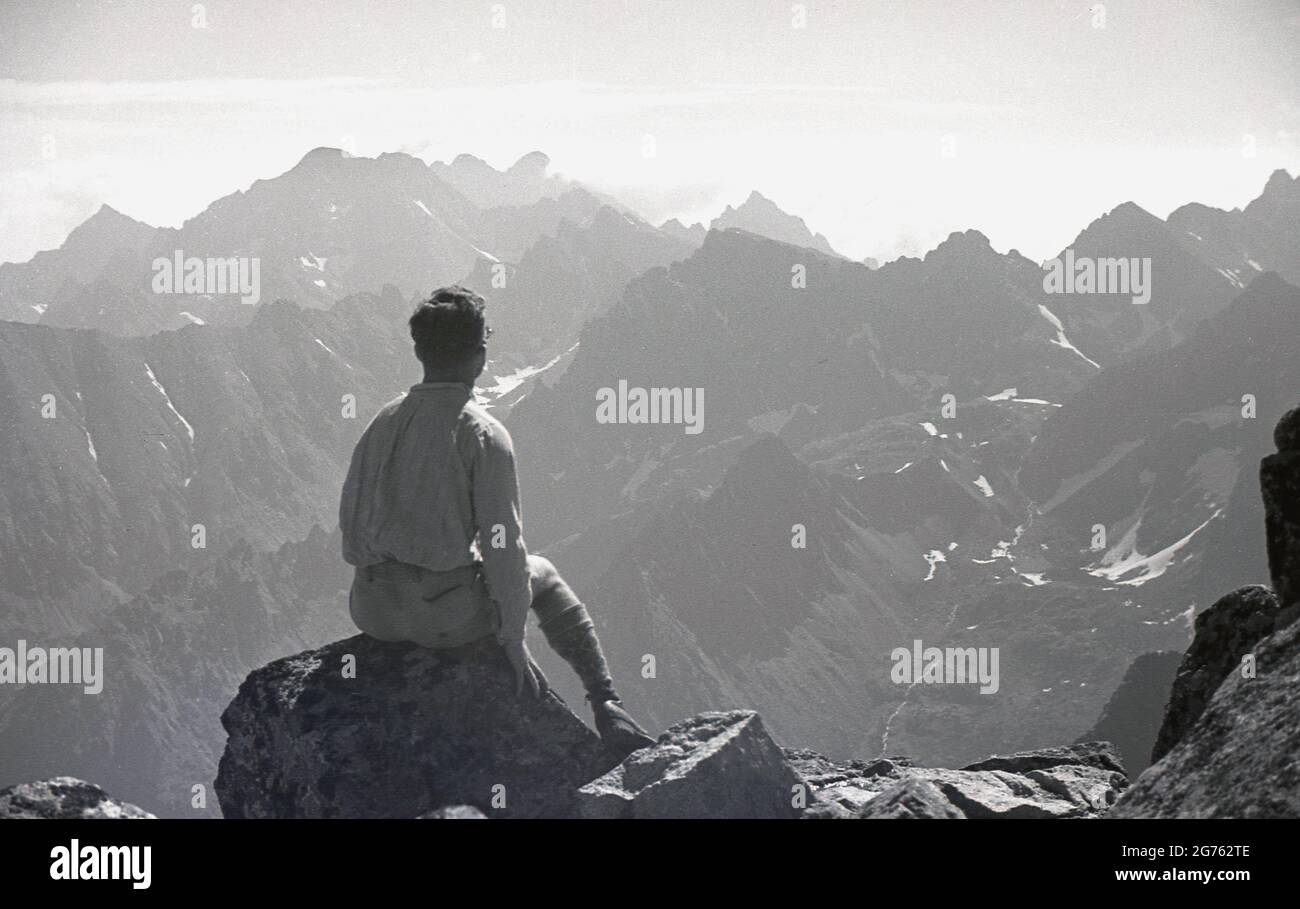 1935, historisch, ein männlicher Wanderer, der auf einem Felsen sitzt und die Aussicht auf die Sudetenberge oder Sudetenberge in der Tschechoslowakei vor dem 2. Weltkrieg überblickt, wobei die höchste Erhebung der Berg Snezka ist. Zu dieser Zeit befanden sich die einzelnen Bergketten und Massive in einer Region, die als Sudetenland bekannt war, einem Gebiet, in dem die Mehrheit der deutschsprachigen Völker beheimatet war. 1938 wurde das Sudetenland über den Münchner Pakt an Deutschland annektiert. Der 2. Weltkrieg begann ein Jahr später. Stockfoto