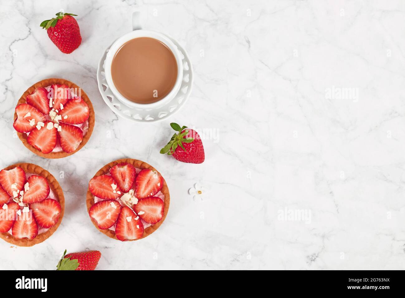 Kleine Tartlet-Gebäckstücke mit Erdbeerfrüchten und weißen Schokoladenstreuseln neben Kaffeetasse und Kopierfläche Stockfoto