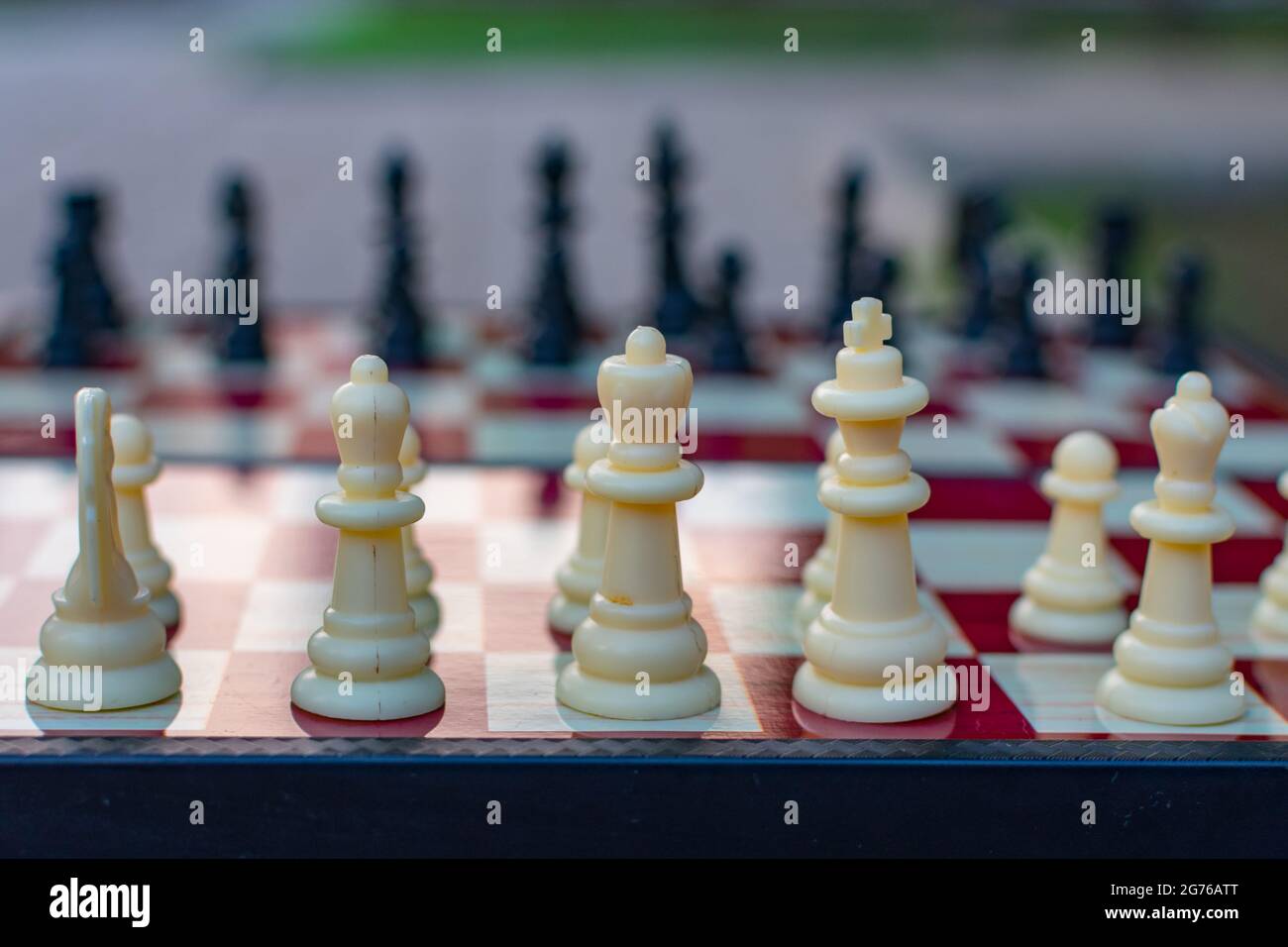 Schachfiguren werden auf einem Schachbrett auf einem unscharfen Hintergrund der Natur platziert. Unscharfer Fokus. Unschärfe-Effekte. Shehamat Tag. Stockfoto