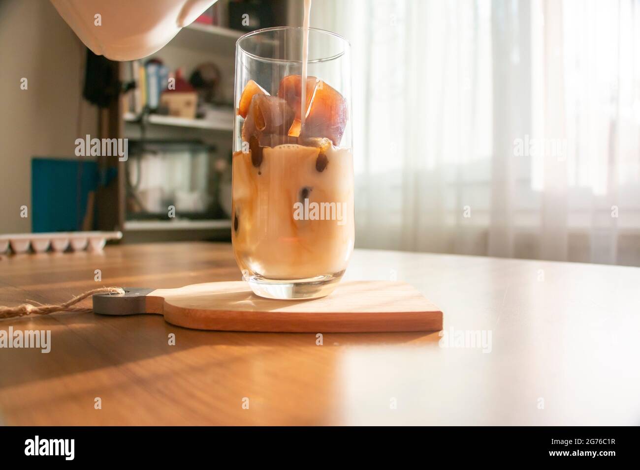 Ein erfrischendes Getränk zubereiten, indem Sie Eiswürfel aus Kaffee zubereiten und Milch in ein Glas gießen. Ein erfrischendes Getränk kalten Kaffee an einem Sommermorgen. Stockfoto