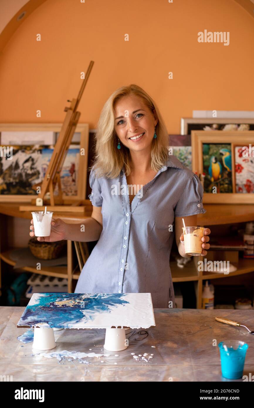 Die schöne Künstlerin in ihrem Studio zeigt den Prozess der Bilderbildung. Innenlackierung. Glück und Kreativität. Hobbys und Kunsthandwerk. Kunstwerk Stockfoto