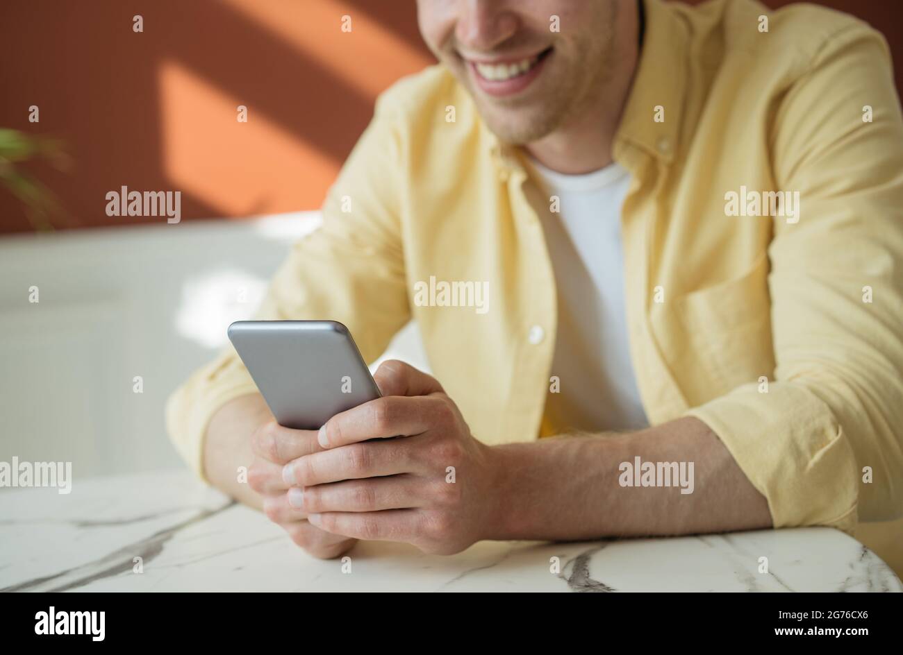 Ein junger lächelnder Mann, der online über ein Mobiltelefon einkaufen und im Café eine Reservierung vornehmen konnte. Glücklicher Freiberufler, der von zu Hause aus arbeitet Stockfoto