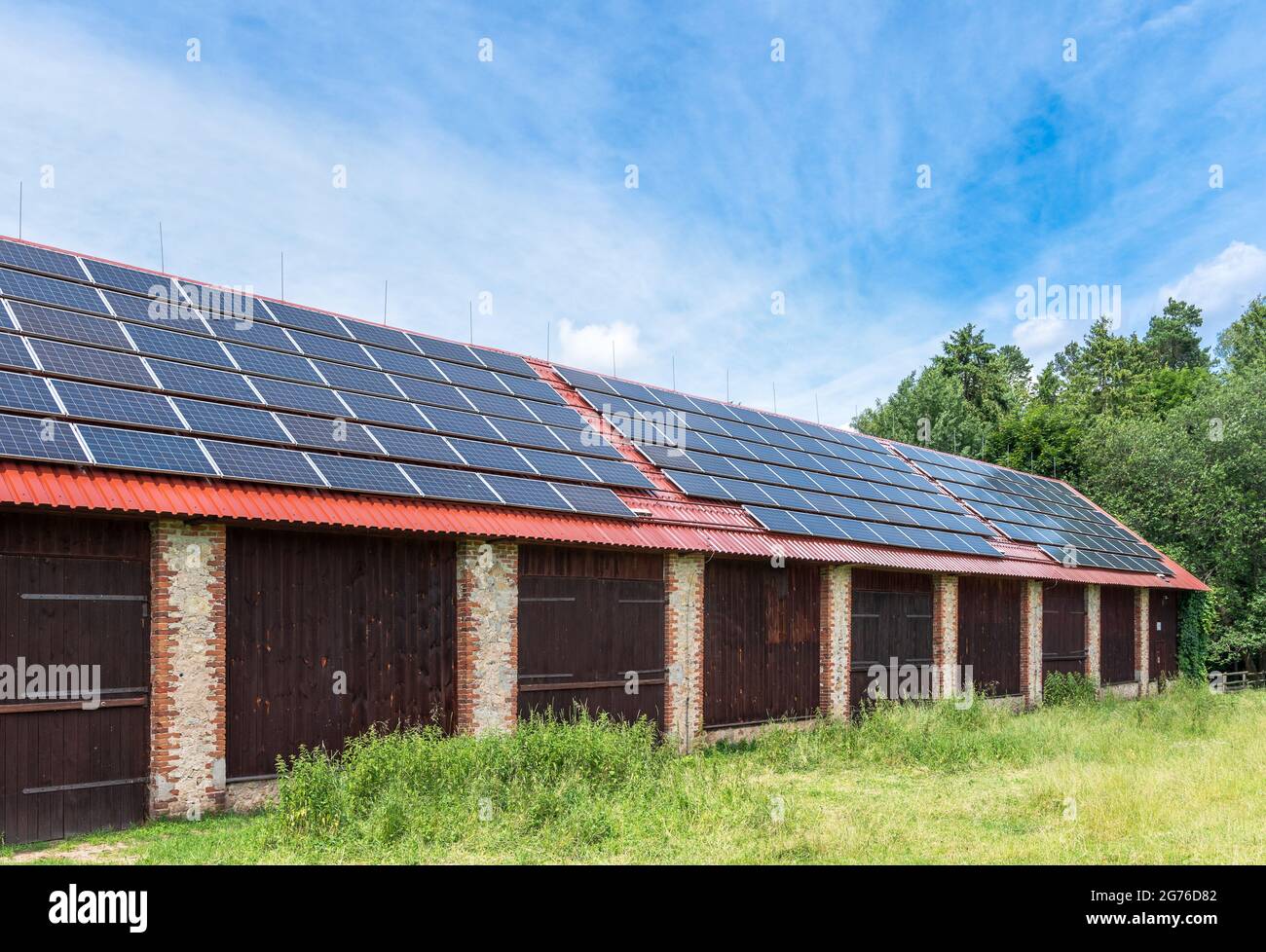 Ziegelscheune in einer Landschaft. Solarpaneele auf dem Dach der Scheune installiert. Stockfoto