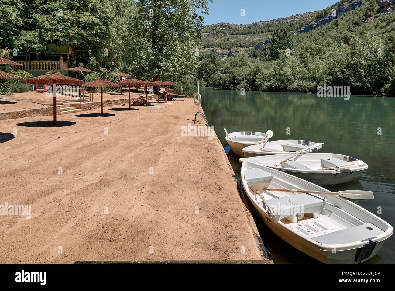 Künstlicher Strand mit weißen Booten, Holzschirmen, Bäumen und Sand am Jucar-Fluss in der Stadt Cuenca, Castilla la Mancha, Spanien, Europa Stockfoto