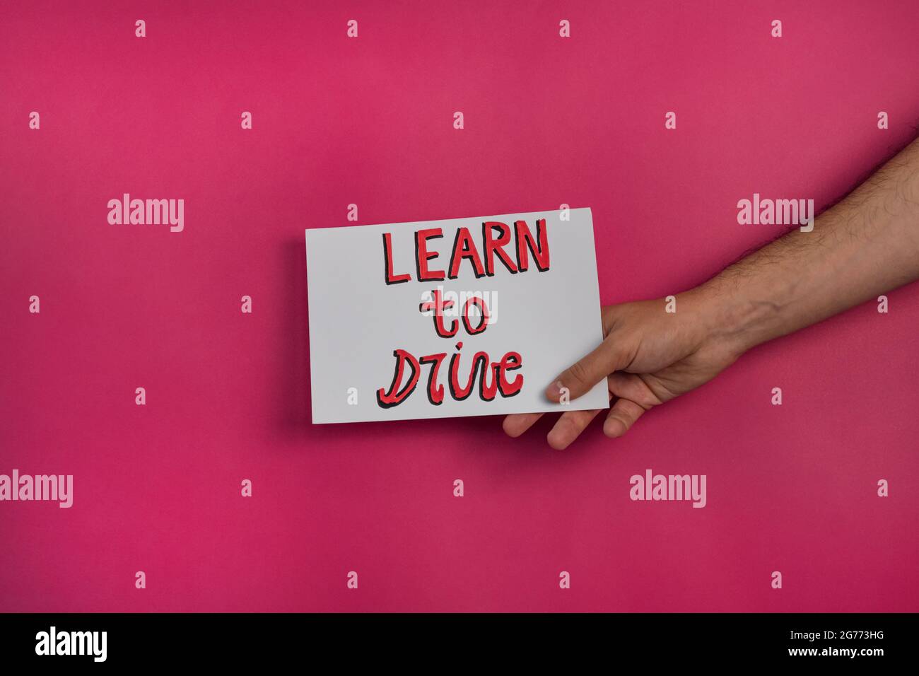 Nahaufnahme eines Mannes, der ein Papier mit dem Wort „AUTOFAHREN LERNEN“ auf einem fuchsienfarbenen Hintergrund hält Stockfoto