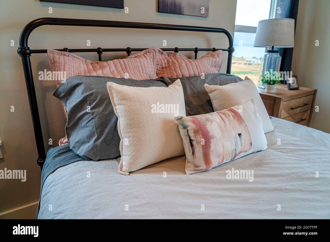 Gemütliches Bett mit schwarzem Metallrahmen und flauschigen Kissen im Schlafzimmer eines Hauses Stockfoto