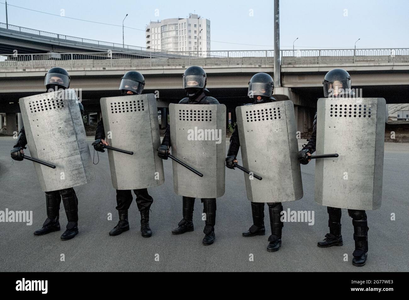 Eine Gruppe von Polizeiwachen mit Helmen, die einen seitlichen Schlagstock und Metallschilde in Reihe auf der Straße halten Stockfoto